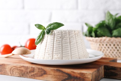 Fresh ricotta (cream cheese) with basil and spoon on white table, closeup