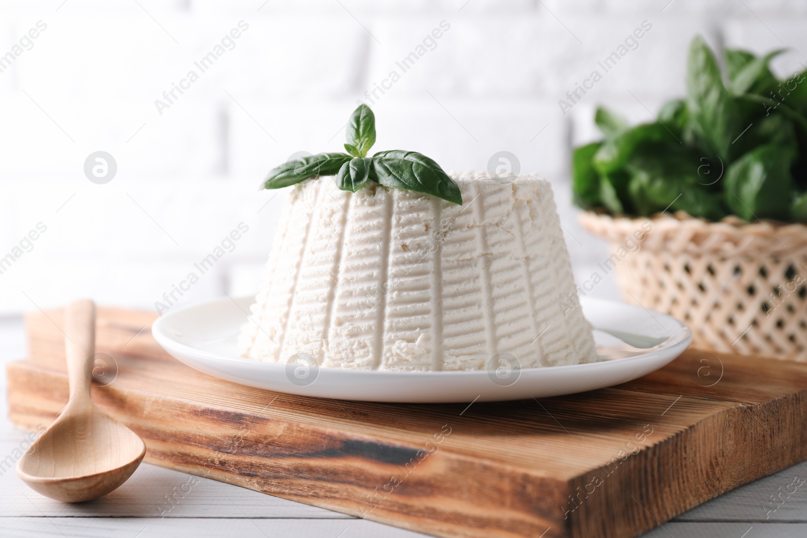 Photo of Fresh ricotta (cream cheese) with basil and spoon on white wooden table