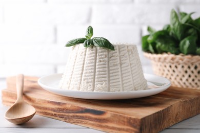 Fresh ricotta (cream cheese) with basil and spoon on white wooden table