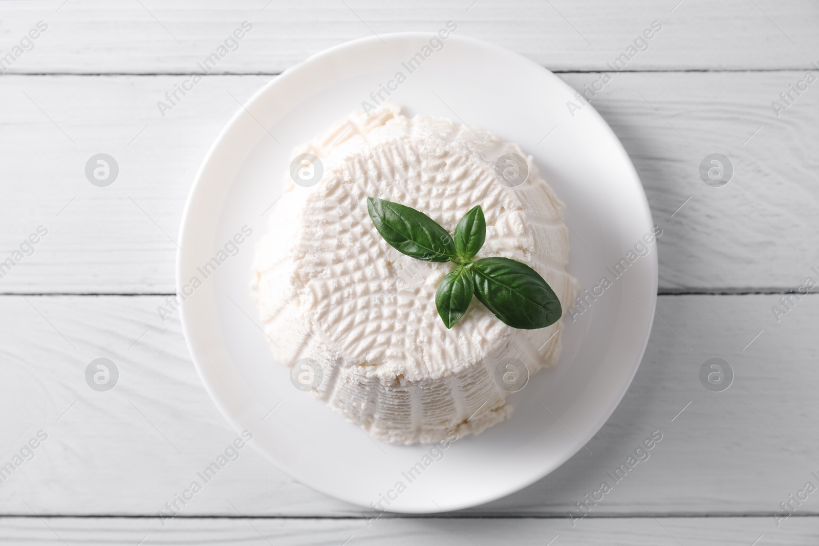 Photo of Fresh ricotta (cream cheese) and basil on white wooden table, top view