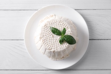 Fresh ricotta (cream cheese) and basil on white wooden table, top view