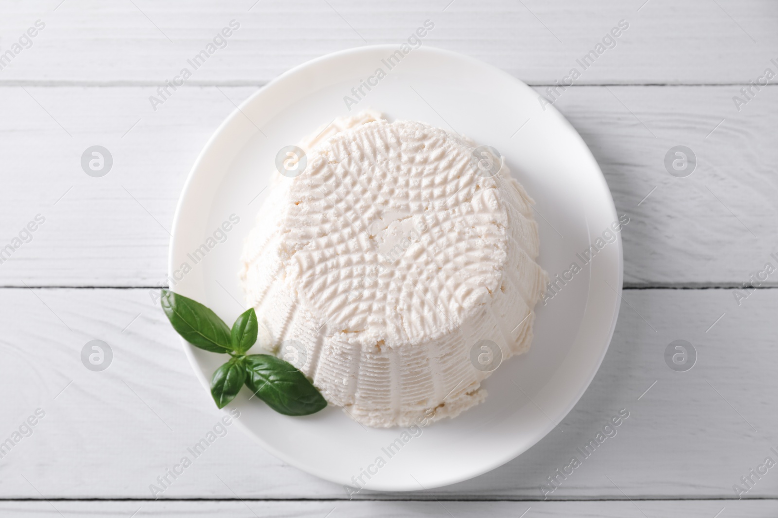 Photo of Fresh ricotta (cream cheese) and basil on white wooden table, top view