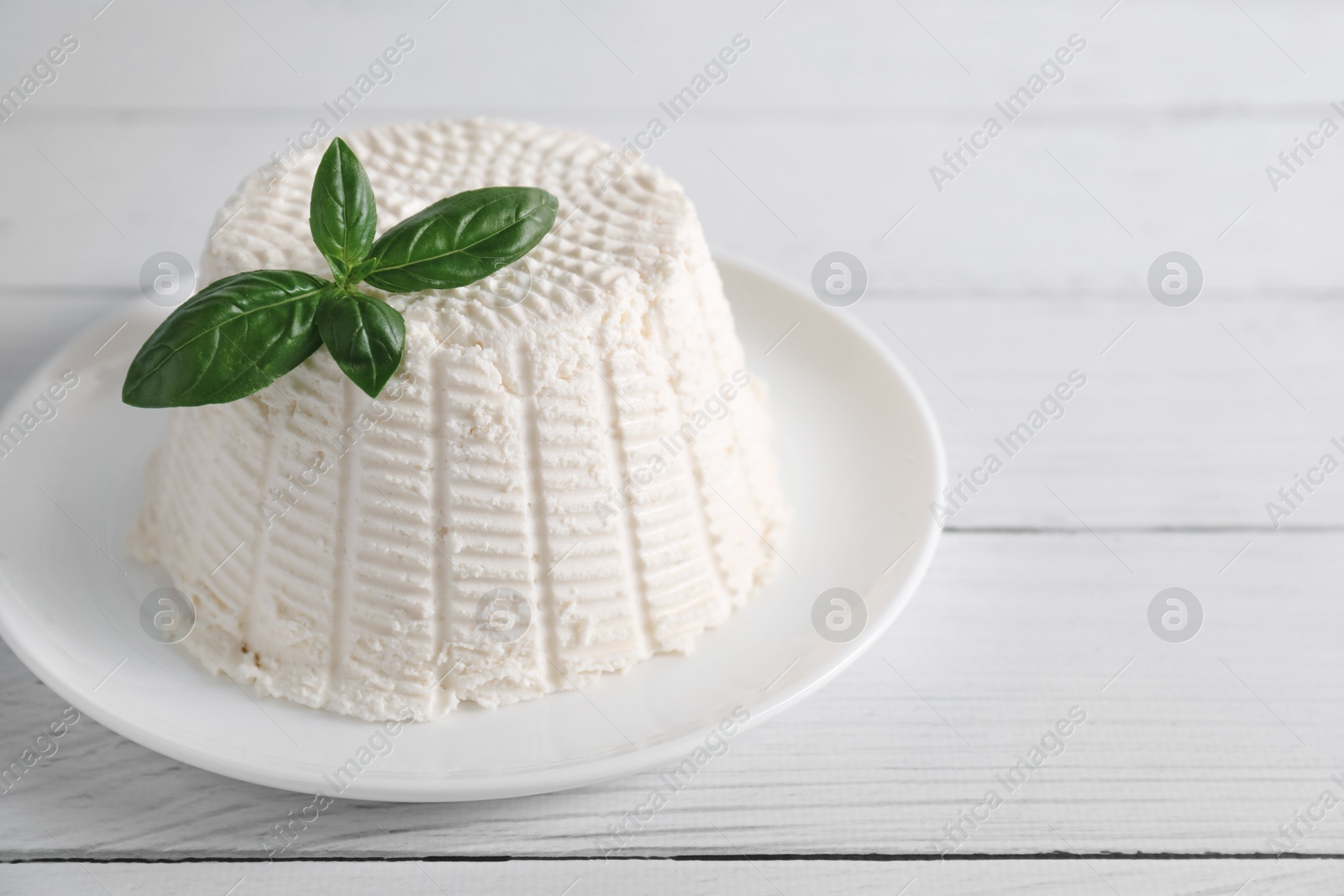 Photo of Fresh ricotta (cream cheese) and basil on white wooden table, space for text