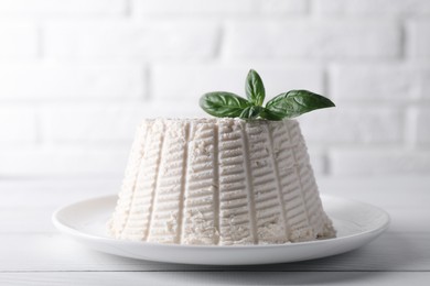 Photo of Fresh ricotta (cream cheese) with basil on white wooden table, closeup