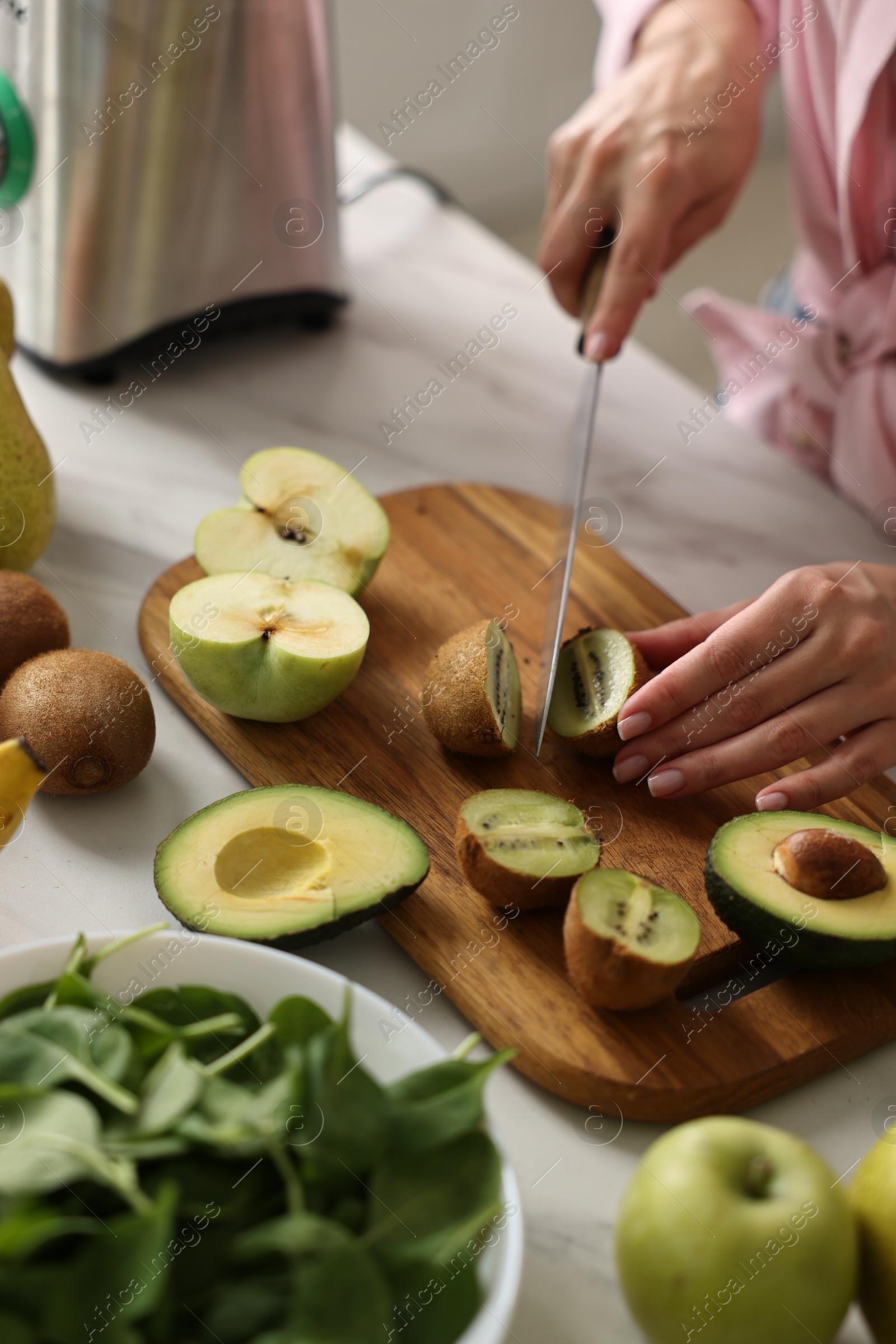 Photo of Woman cutting kiwi for smoothie at white marble table in kitchen, closeup
