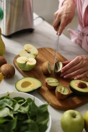 Photo of Woman cutting kiwi for smoothie at white marble table in kitchen, closeup