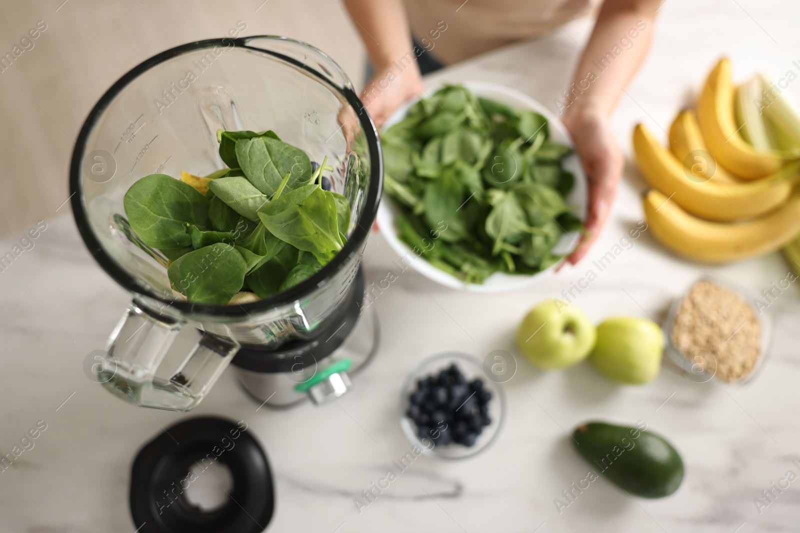 Photo of Woman making delicious smoothie with blender at white marble table in kitchen, above view