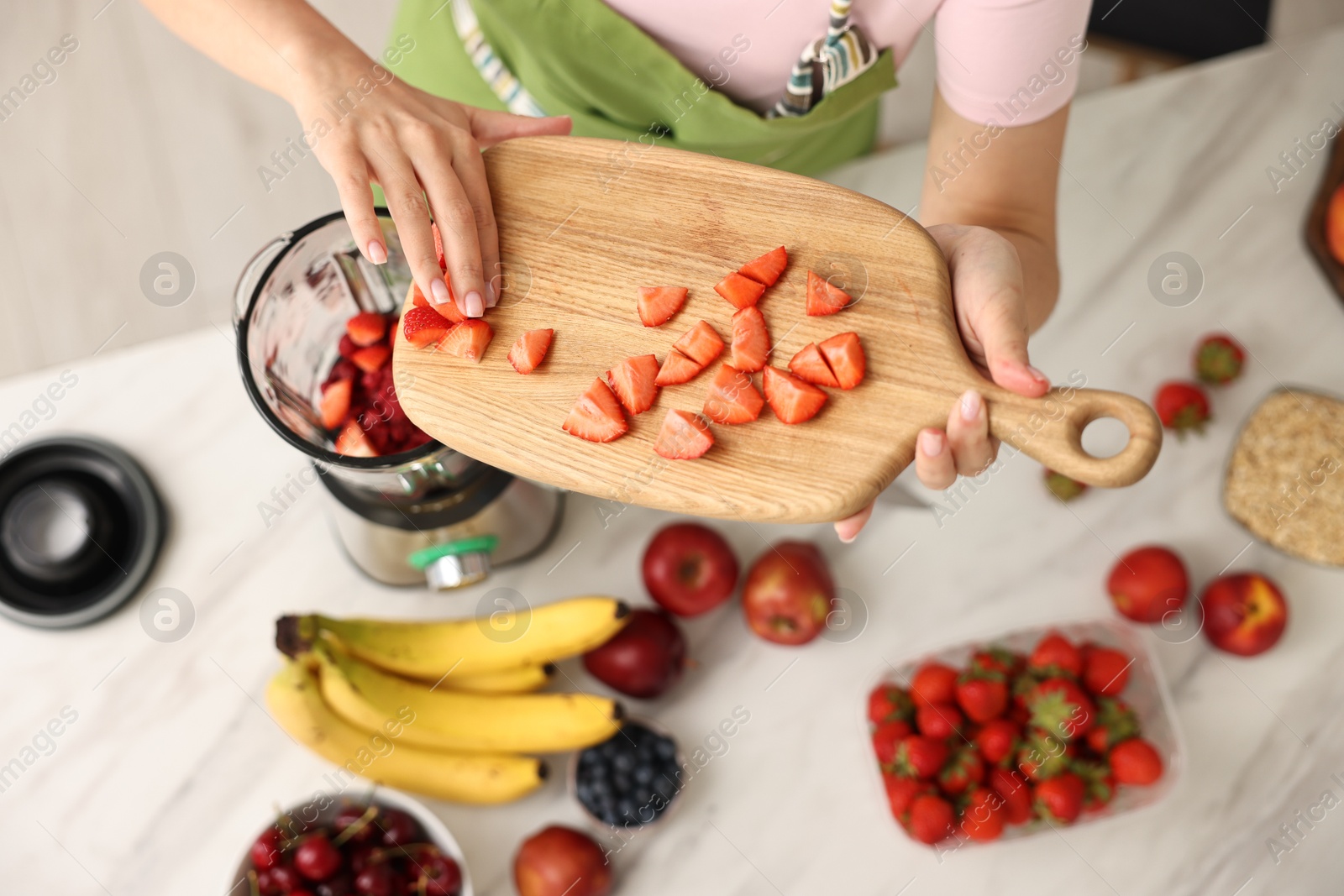 Photo of Woman making delicious smoothie with blender at white marble table in kitchen, above view