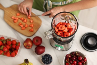 Photo of Woman making delicious smoothie with blender at white marble table in kitchen, above view