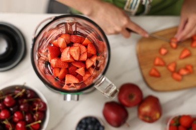 Woman making delicious smoothie with blender at white marble table in kitchen, top view