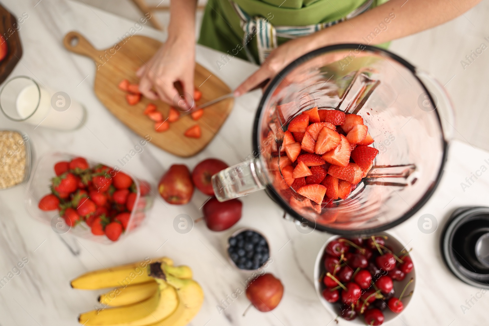 Photo of Woman making delicious smoothie with blender at white marble table in kitchen, top view