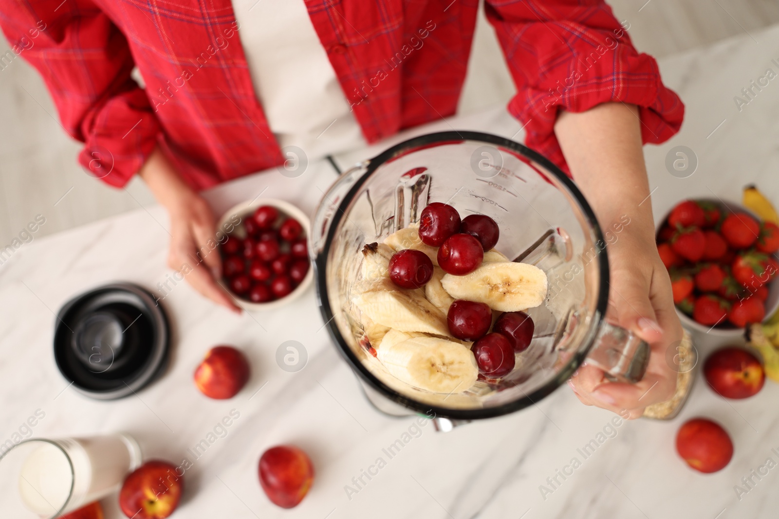 Photo of Woman making delicious smoothie with blender at white marble table in kitchen, above view