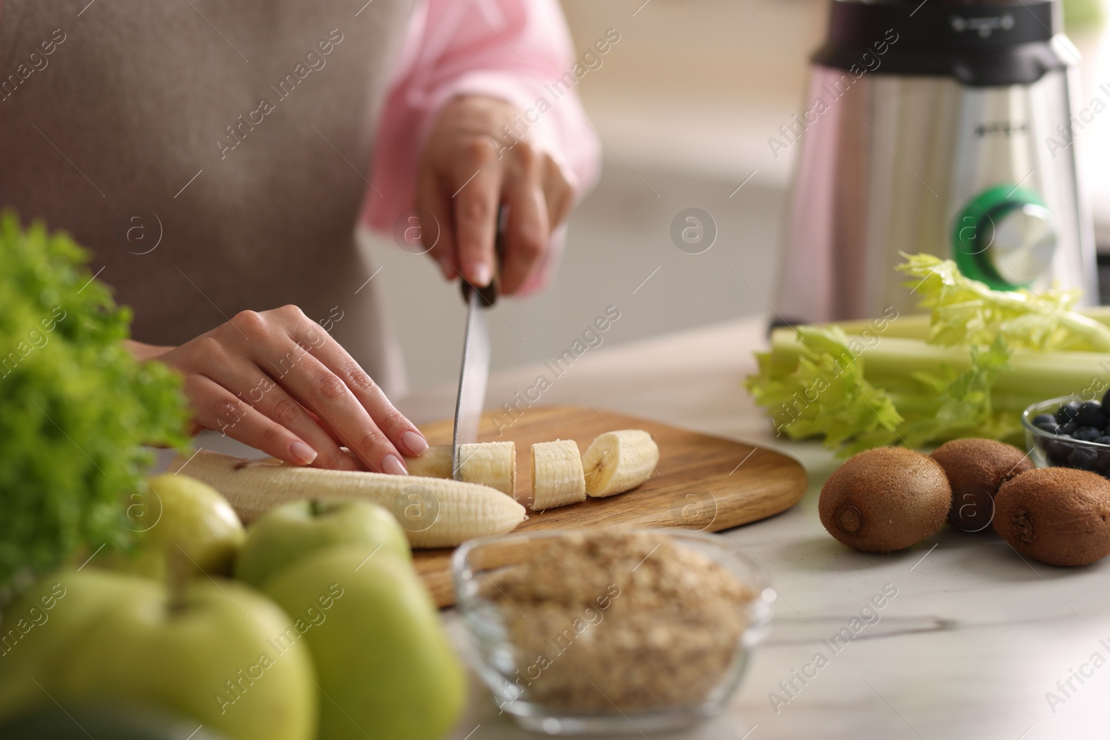 Photo of Woman cutting banana for smoothie at white marble table in kitchen, closeup