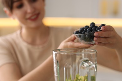 Photo of Young woman making delicious smoothie with blender in kitchen, selective focus