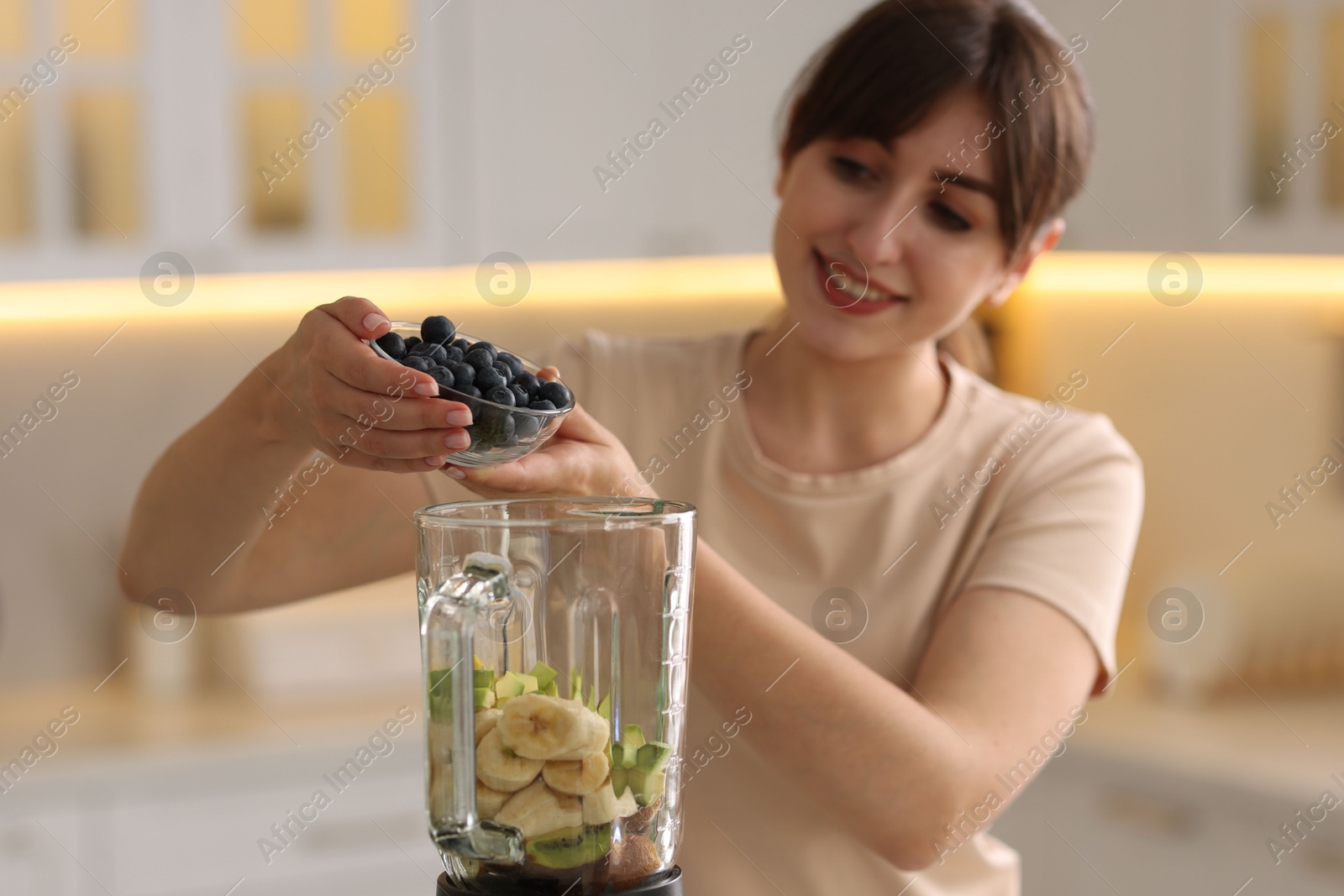 Photo of Young woman making delicious smoothie with blender in kitchen