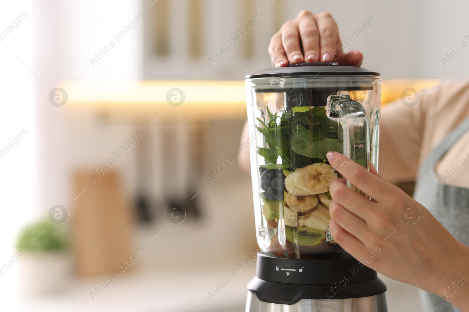 Photo of Woman making delicious smoothie with blender in kitchen, closeup