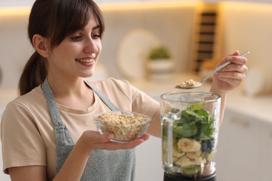 Photo of Young woman making delicious smoothie with blender in kitchen
