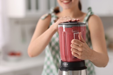 Woman making delicious smoothie with blender in kitchen, closeup