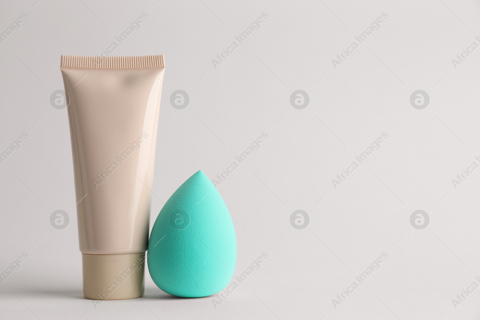 Photo of Makeup sponge and skin foundation on light grey background, space for text