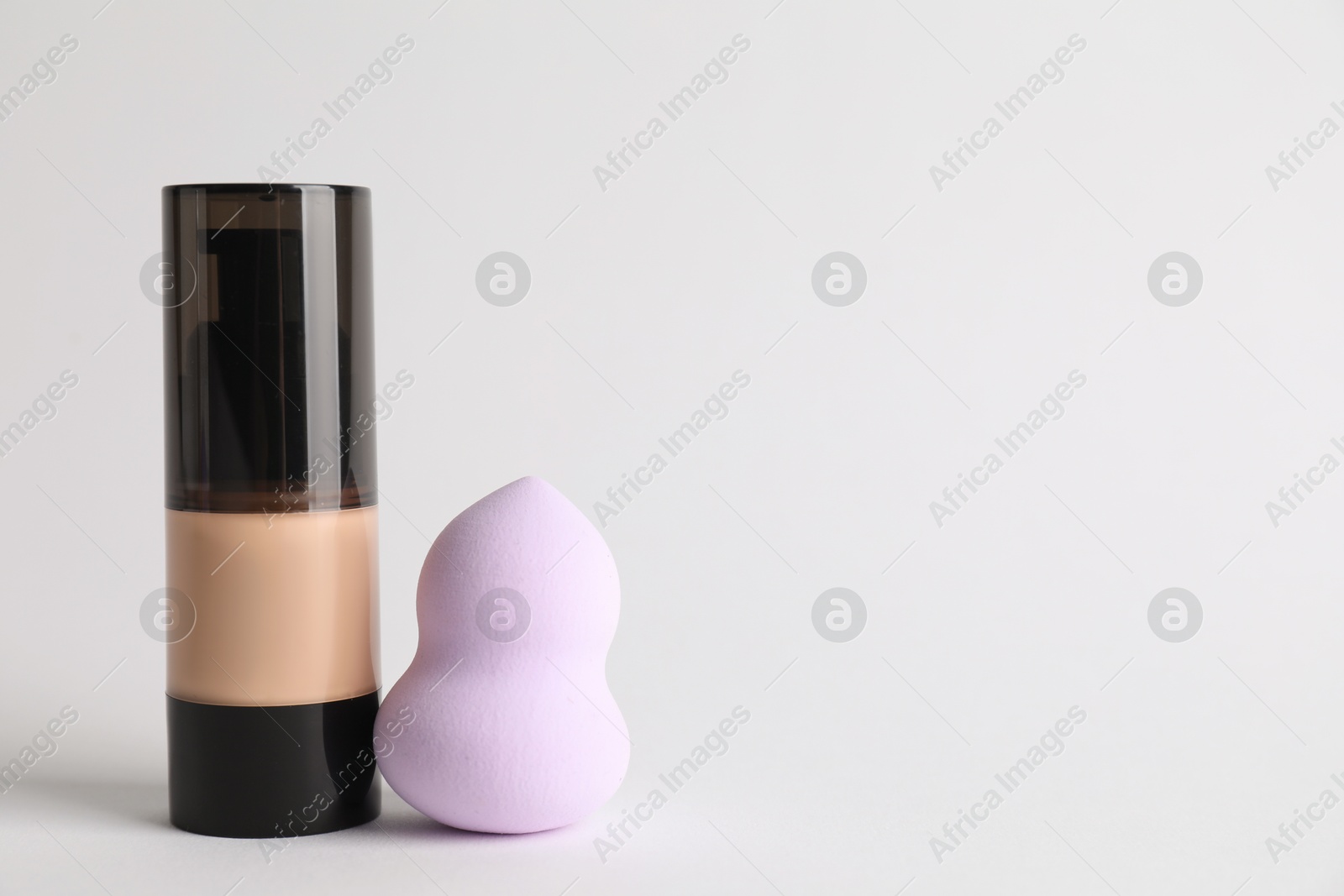 Photo of Makeup sponge and skin foundation on light grey background, space for text