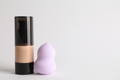 Photo of Makeup sponge and skin foundation on light grey background, space for text