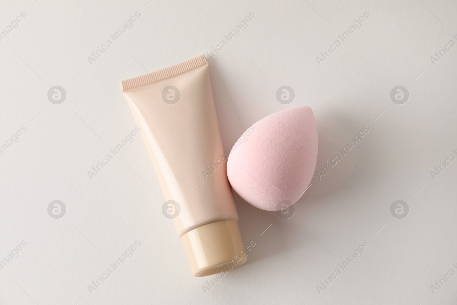 Photo of Makeup sponge and skin foundation on light grey background, top view