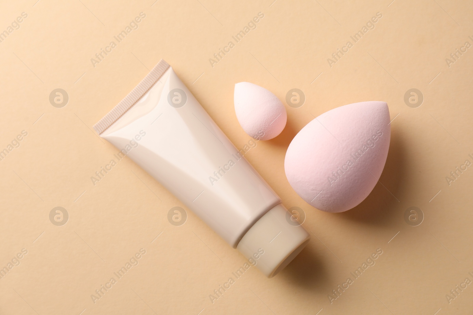 Photo of Makeup sponges and skin foundation on beige background, flat lay