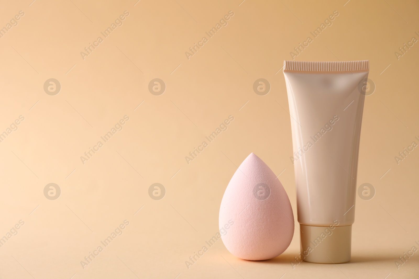 Photo of Makeup sponge and skin foundation on beige background, space for text