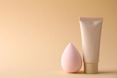 Photo of Makeup sponge and skin foundation on beige background, space for text