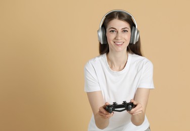 Happy woman in headphones playing video games with controller on beige background