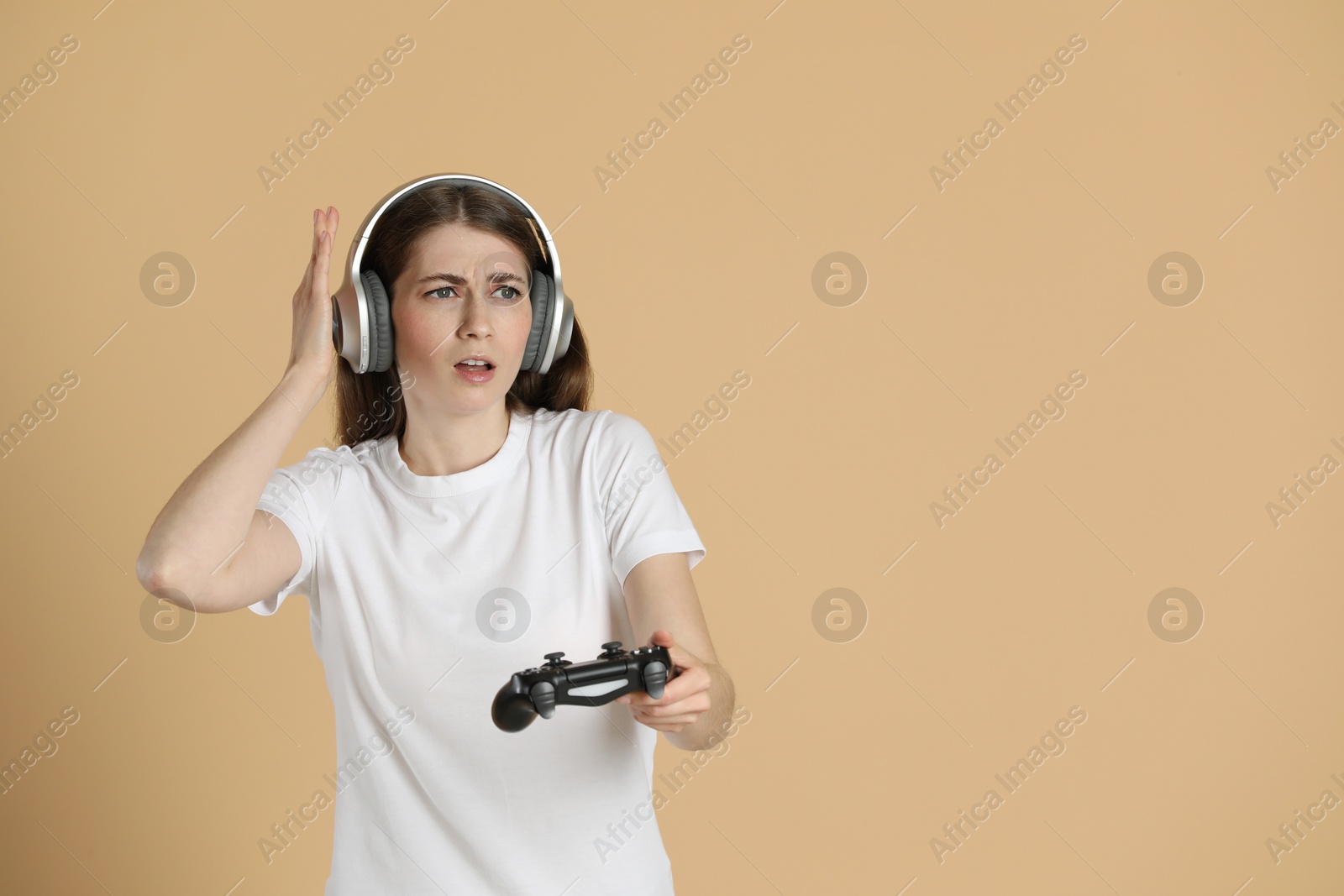 Photo of Woman in headphones playing video games with controller on beige background, space for text