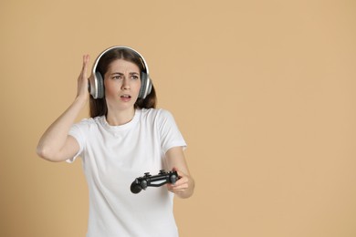 Woman in headphones playing video games with controller on beige background, space for text