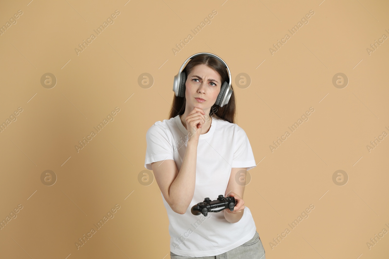 Photo of Thoughtful woman in headphones with controller on beige background