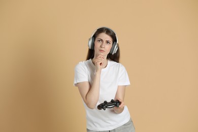 Photo of Thoughtful woman in headphones with controller on beige background