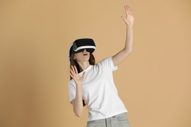 Photo of Surprised woman using virtual reality headset on beige background