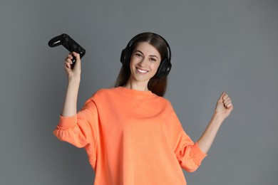 Happy woman in headphones with controller on gray background