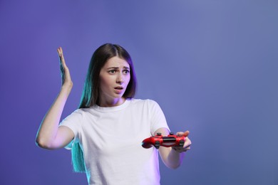 Surprised woman playing video games with controller on violet background