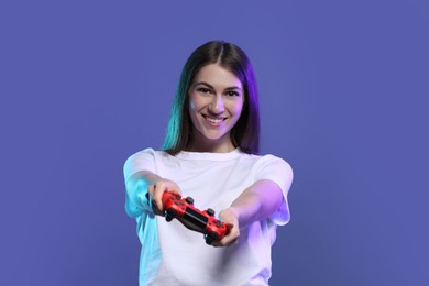 Photo of Happy woman playing video games with controller on violet background