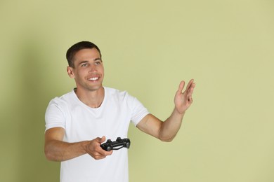 Happy man with controller on light green background, space for text