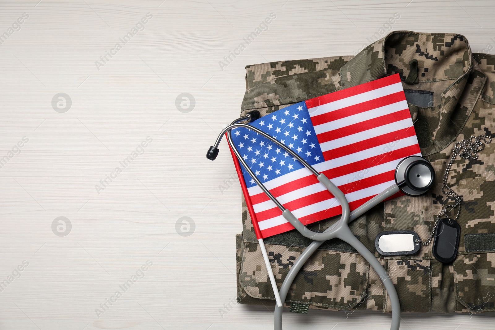 Photo of Stethoscope, USA flag, tags and military uniform on white wooden table, top view. Space for text