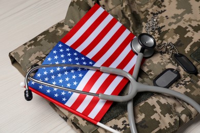 Photo of Stethoscope, USA flag, tags and military uniform on white wooden table