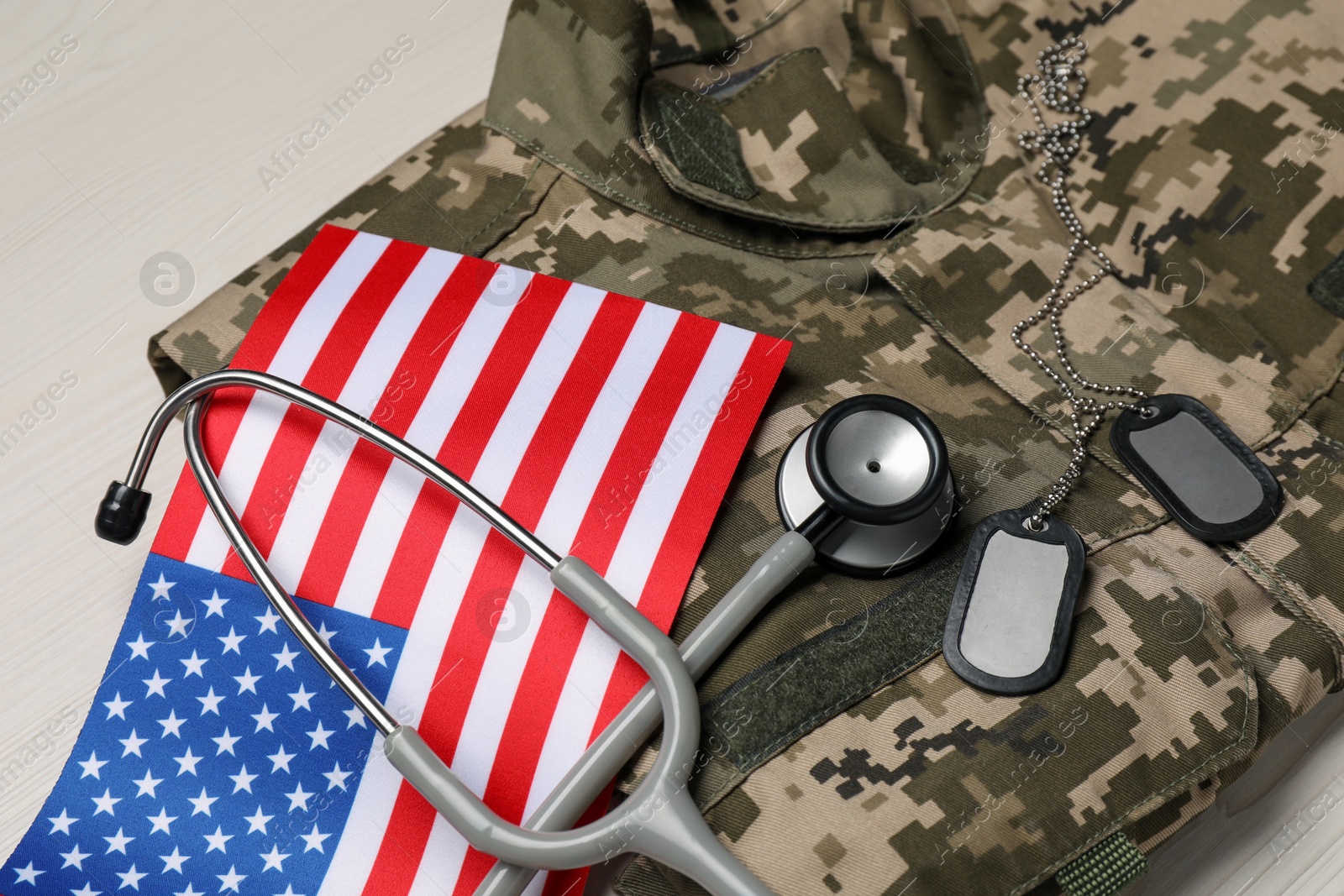 Photo of Stethoscope, USA flag, tags and military uniform on white wooden table