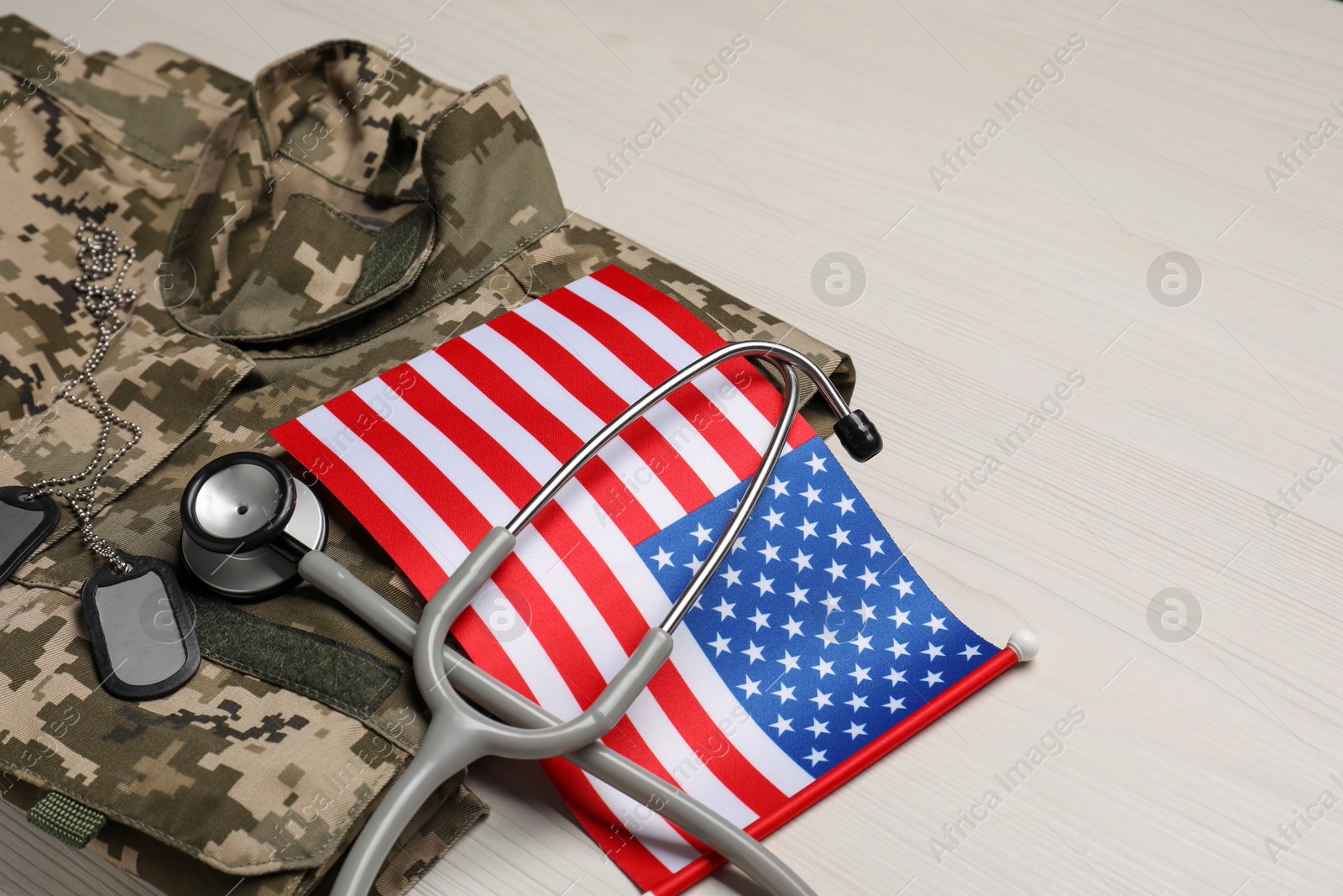 Photo of Stethoscope, USA flag, tags and military uniform on white wooden table