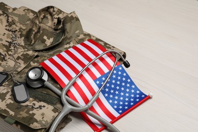 Stethoscope, USA flag, tags and military uniform on white wooden table