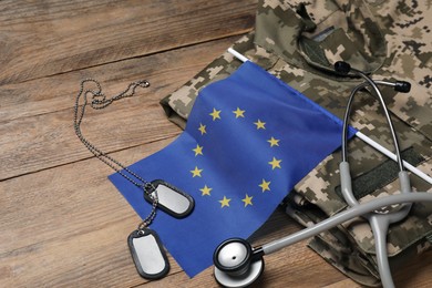 Stethoscope, flag of European Union, tags and military uniform on wooden table