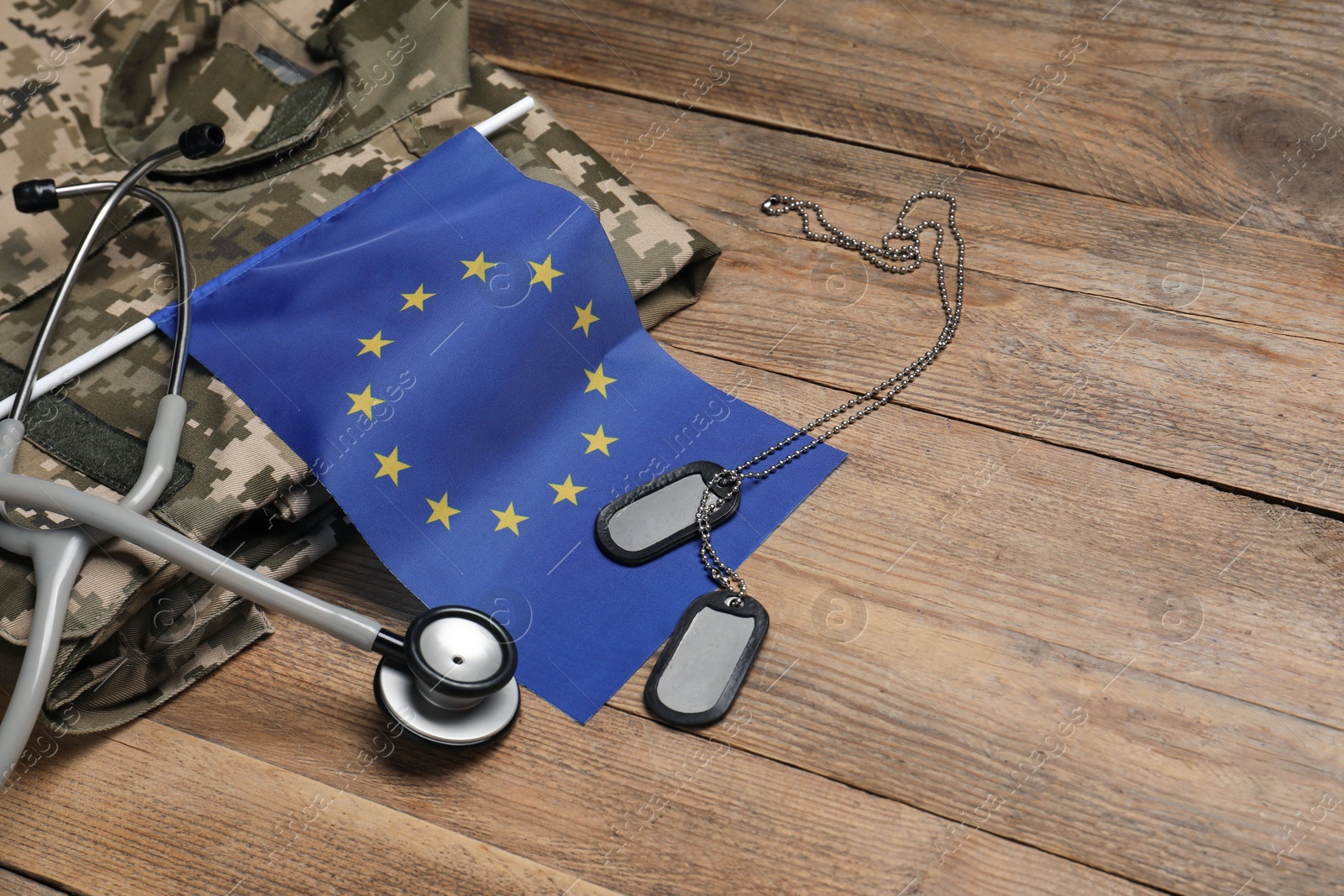 Photo of Stethoscope, flag of European Union, tags and military uniform on wooden table. Space for text