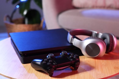 Video game console, wireless controller and headphones on wooden table indoors