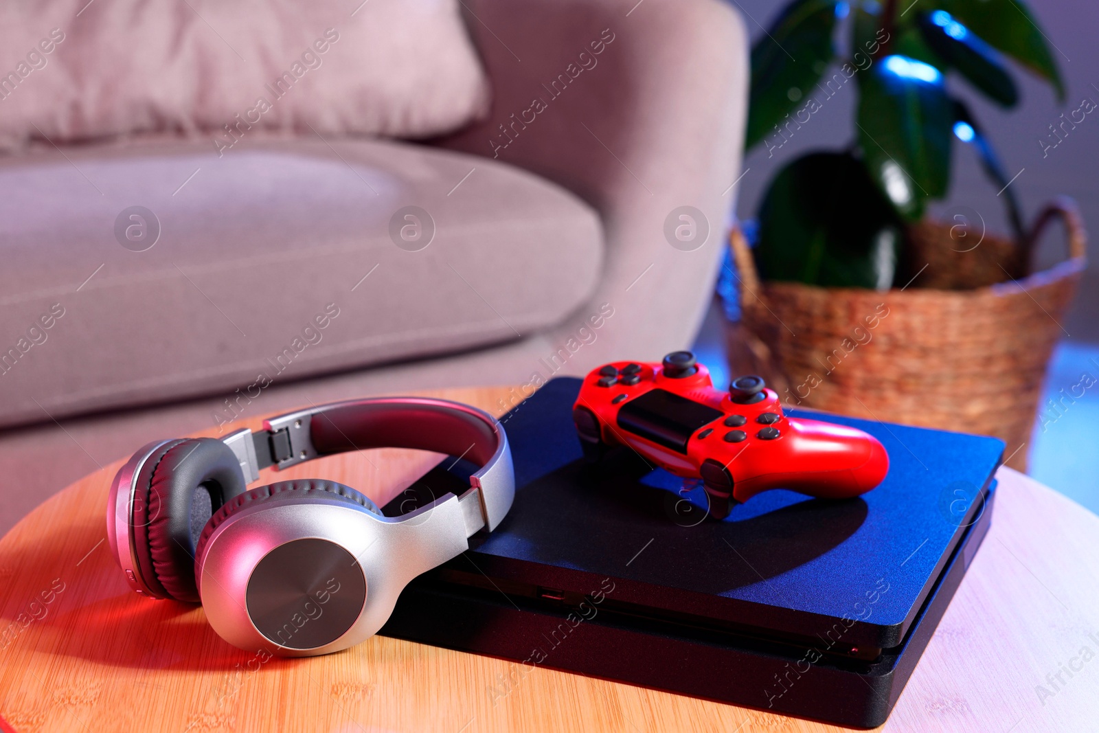 Photo of Video game console, wireless controller and headphones on wooden table indoors