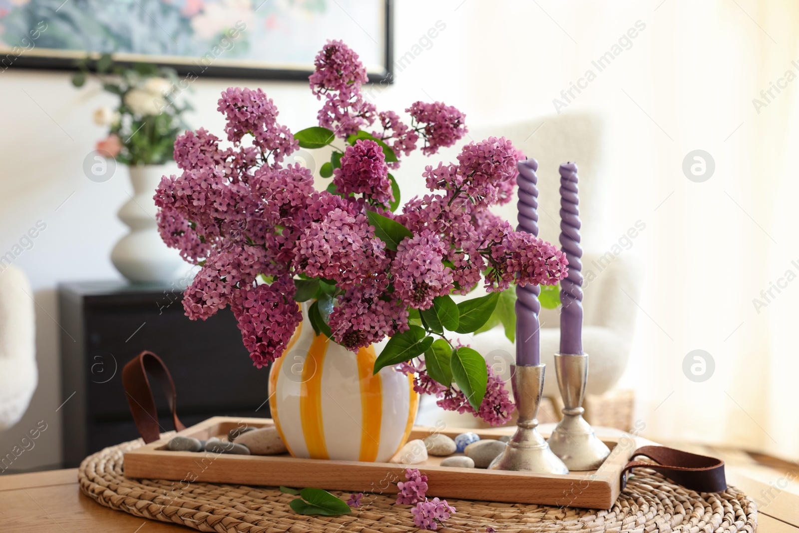 Photo of Beautiful lilac flowers in vase and candles on table at home