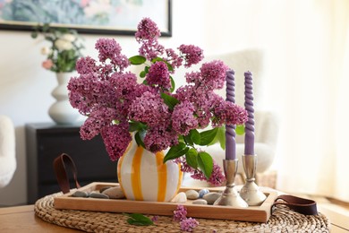 Beautiful lilac flowers in vase and candles on table at home